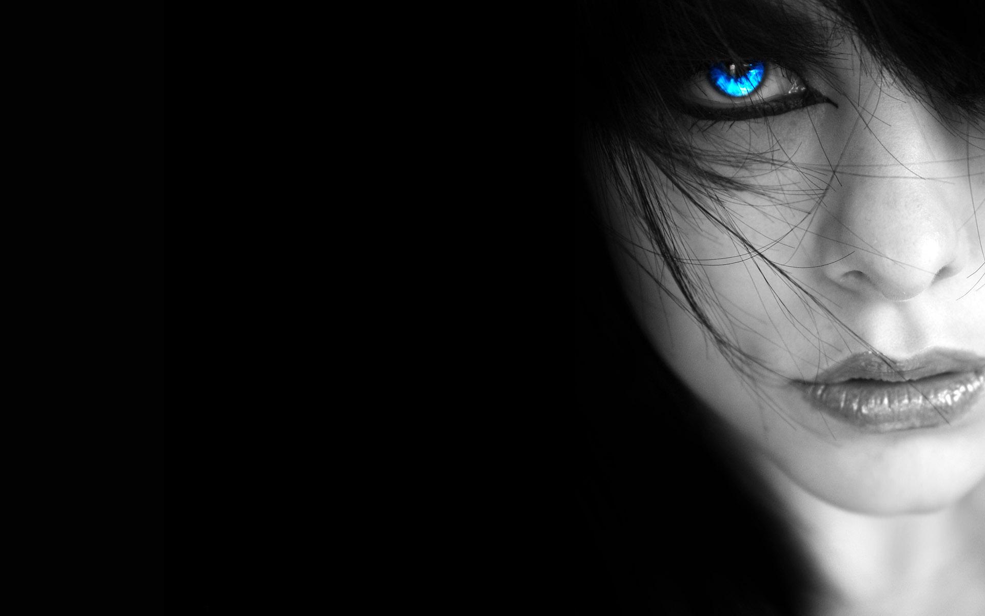 Black-and-white portrait of a woman with hair across her face and one vivid electric-blue eye, set against deep black